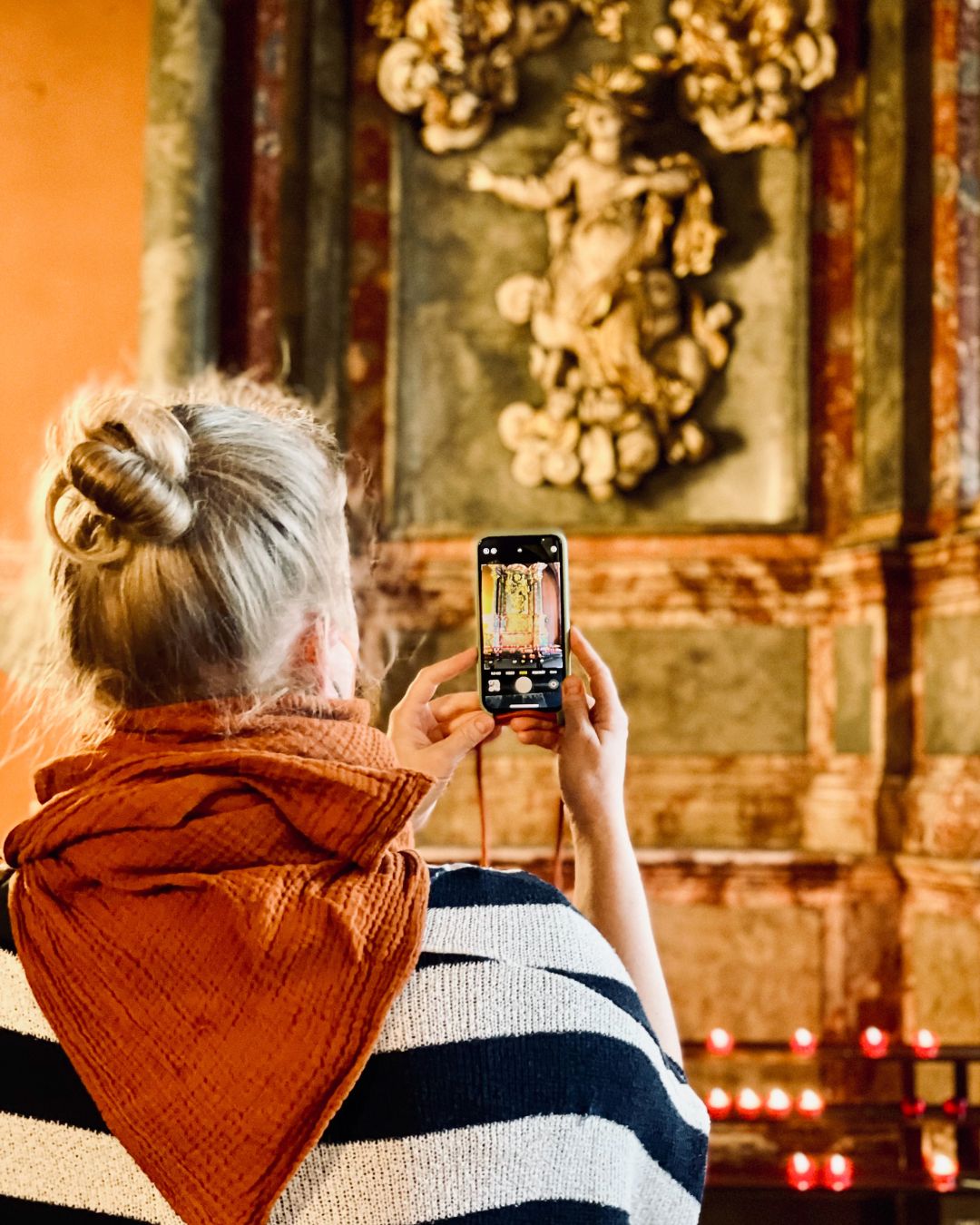 Eine Frau steht mit dem Handy in einer Kirche vor dem Altar und macht Fotos. Sie ist von hinten zu sehen, das Bild auf dem Handy ist scharf.